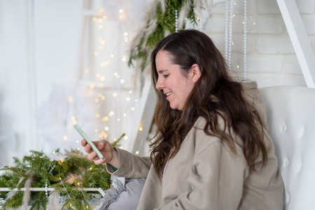 Woman smiling using phone near christmas decorationsの写真素材