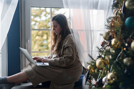 Woman using laptop in living room with Christmas decorations. Buying gifts, working from homeの写真素材
