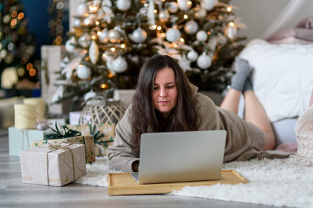 Woman using laptop in living room with Christmas decorations. Buying gifts, working from homeの写真素材
