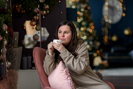 Woman drinking coffee or tea near christmas decorations sitting on chairの写真素材