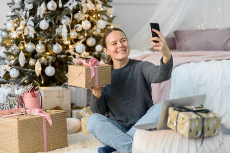 Woman with laptop, Christmas gifts and decorations. Buying or ordering online, making selfie with phone and boxの写真素材