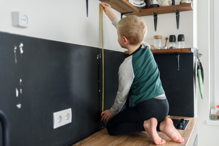 Boy child using metal tape measure to renovation works at home kitchenの写真素材