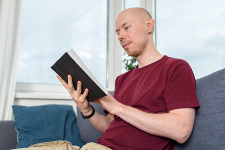 Bald hairless man reading book sitting on couch