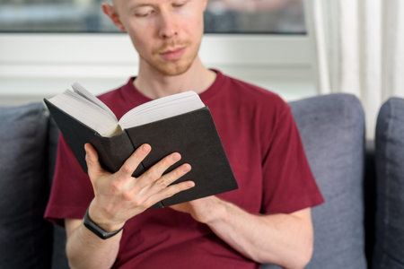 Bald hairless man reading book sitting on couch