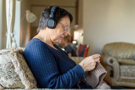 Mature woman in headphones knitting hat, listening to music and relaxingの写真素材