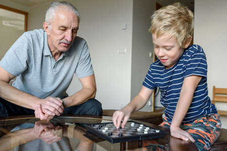 Grandfather with little grandson playing board game checkers at homeの写真素材