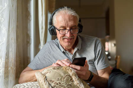 Senior man in headphones listening to music from mobile phone and smilingの写真素材