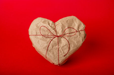 Heart-shaped gift box wrapped in kraft paper on red backgroundの写真素材
