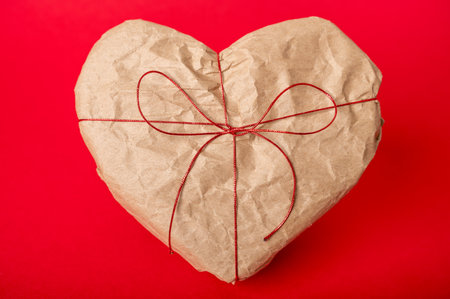 Heart-shaped gift box wrapped in kraft paper on red backgroundの写真素材