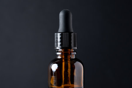 Bottle with liquid transparent gel, serum or essential oil on black. With glass pipette insideの写真素材