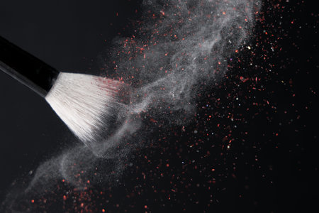 Makeup brush with crushed white floating powder and red glitter on black backgroundの写真素材