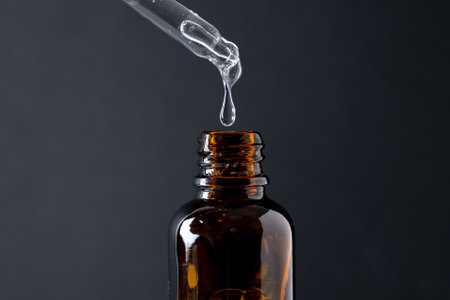 Pipette with liquid transparent gel, serum or essential oil on black. With glass bottleの写真素材