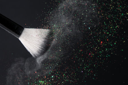 Makeup brush with crushed white floating powder and red green glitter on black backgroundの写真素材