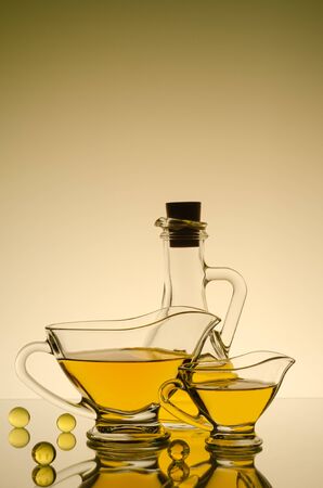 Large and small glass transparent saucers with yellow transparent sauce, behind a glass transparent oiler with yellow oil. White background, at the top of the frame a gradient with dimming.の写真素材