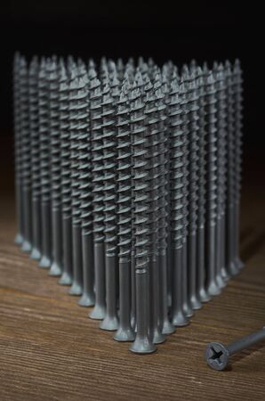 Gray self-tapping screws stand in the shape of a triangle on a wooden table, next to it is a screw, vertical orientation of the frameの写真素材