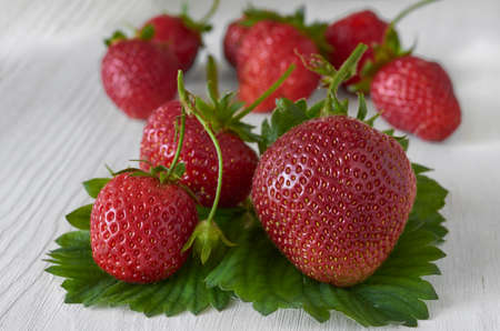 Fresh strawberries with leaves close-up on a white wooden table.の写真素材