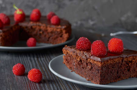 Piece of chocolate muffin with bright red berries close-up.In the background a dish with a whole muffin.Low key.の写真素材