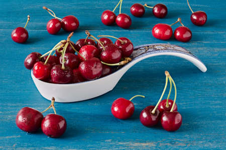 Fresh cherries on a blue wooden table, some in a ceramic dipper.