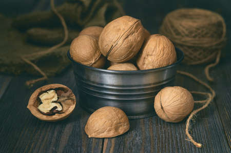 A small metal bowl of walnuts stands on a dark wooden table, with burlap and twine in the shade in...