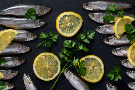 Small fish lie on a dark slate dish with sliced lemon and fresh parsley. view from above.の写真素材