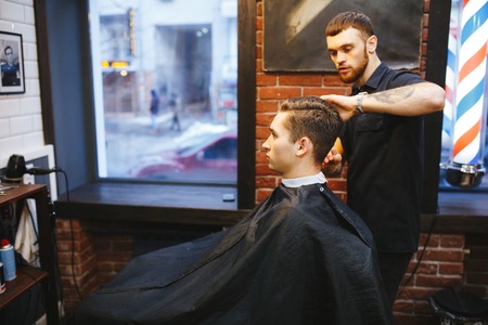 Master cuts hair of men in the barbershop, hairdresser makes hairstyle for a young man