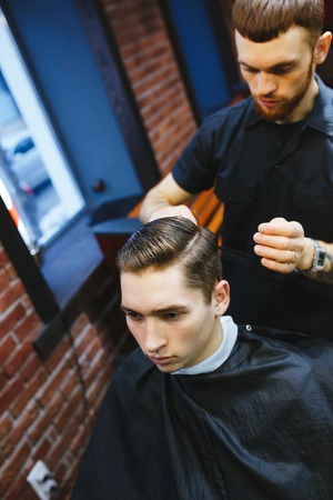 Master cuts hair of men in the barbershop, hairdresser makes hairstyle for a young manの写真素材