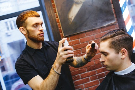 Master cuts hair of men in the barbershop, hairdresser makes hairstyle for a young manの写真素材