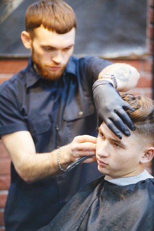 Hairdresser shaving young man with a straight razorの写真素材