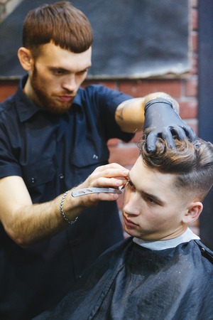 Hairdresser shaving young man with a straight razorの写真素材