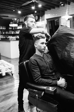 Master cuts hair of men in the barbershop, hairdresser makes hairstyle for a young manの写真素材