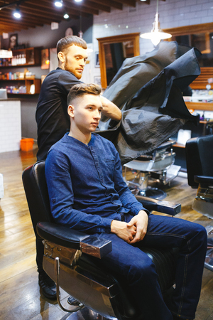 Master cuts hair of men in the barbershop, hairdresser makes hairstyle for a young manの写真素材