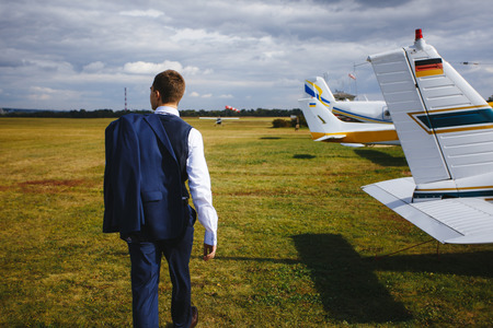 Serious handsome young man in the west and suit walk near small plane on the airfield.の写真素材