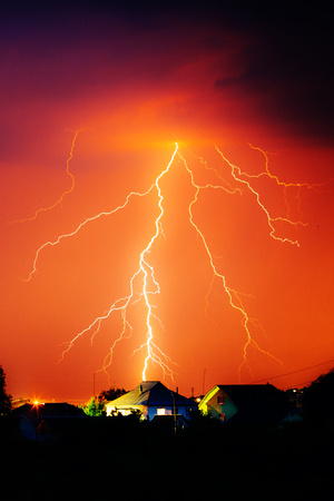 Cloud to Ground Electric Lightning behind house roof tops.