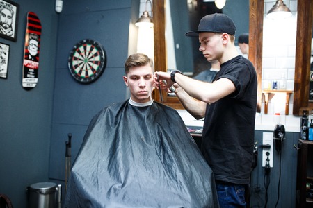 Master cuts hair of men in the barbershop, hairdresser makes hairstyle for a young man.