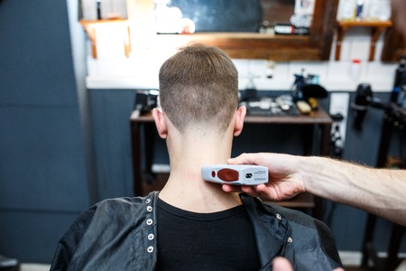 Young handsome barber making haircut of attractive man in barbershop.の写真素材