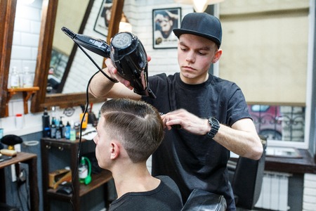 Master cuts hair of men in the barbershop, hairdresser makes hairstyle for a young man.の写真素材