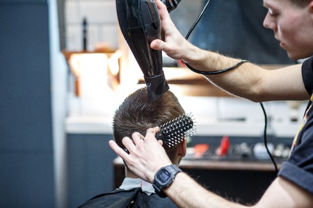 Great time at barbershop. Cheerful young bearded man getting haircut by hairdresser while sitting in chair at barbershop.の写真素材