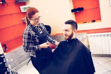female hairdresser is cutting hair of bearded man client.の写真素材