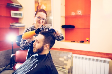 female hairdresser is cutting hair of bearded man client.の写真素材