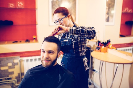 female hairdresser is cutting hair of bearded man client.の写真素材