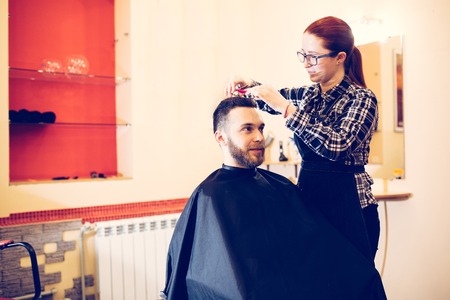 female hairdresser is cutting hair of bearded man client.の写真素材