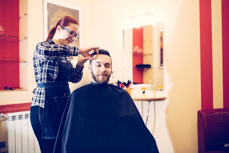 female hairdresser is cutting hair of bearded man client.の写真素材