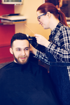 female hairdresser is cutting hair of bearded man client.の写真素材