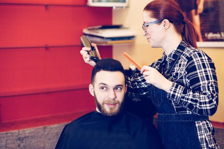 female hairdresser is cutting hair of bearded man client.の写真素材
