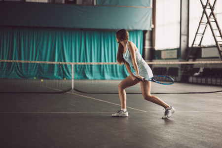Full body portrait of young girl tennis player in action in a tennis court indoor.の写真素材