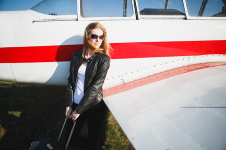 Beautiful woman in black leather jacket standing in front of small vintage aircraft.の写真素材