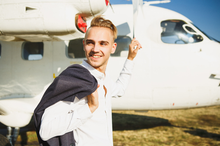 A young smiling man stands near an airplane. Small aircraft for private travel.の写真素材