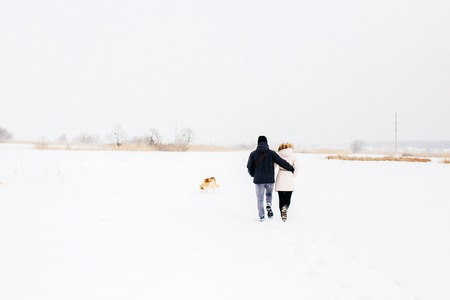 A young couple walking in the woods with the dog red husky with blue eyes. Snowy morning in the forest. A girl and a guy dressed in warm clothesの写真素材