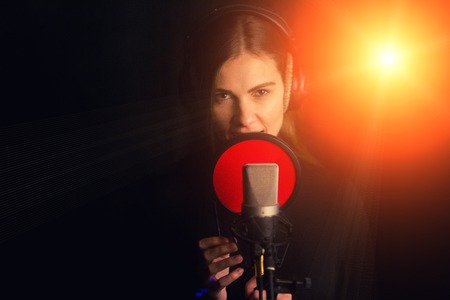 Singing girl sing to the professional microphone in the record studio. Process of create a new hit song by young singer.の写真素材