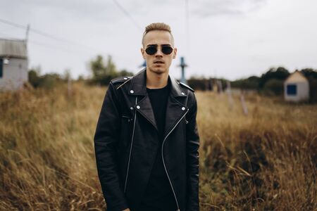 Young sexy man in leather jacket and sunglasses standing outdoorの写真素材